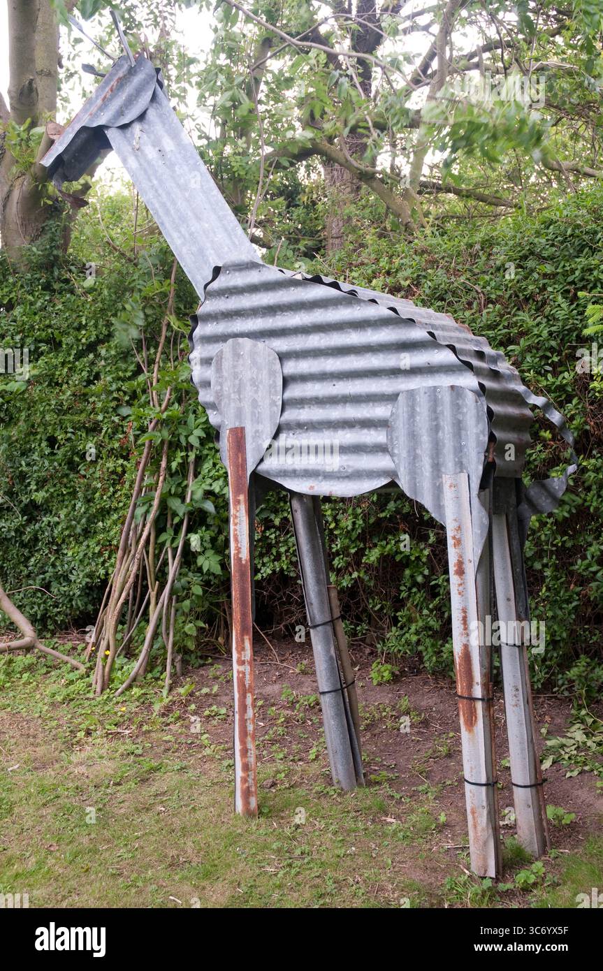 Una grande scultura di giraffa in metallo si erge alto tra la vegetazione lussureggiante in un giardino, mostrando arte creativa in un ambiente naturale. Foto Stock