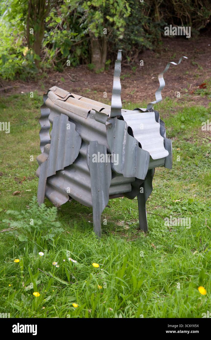 Una scultura creata in modo creativo che prende la forma di una capra si distingue in un vibrante giardino, circondato da lussureggianti alberi e erba. Foto Stock