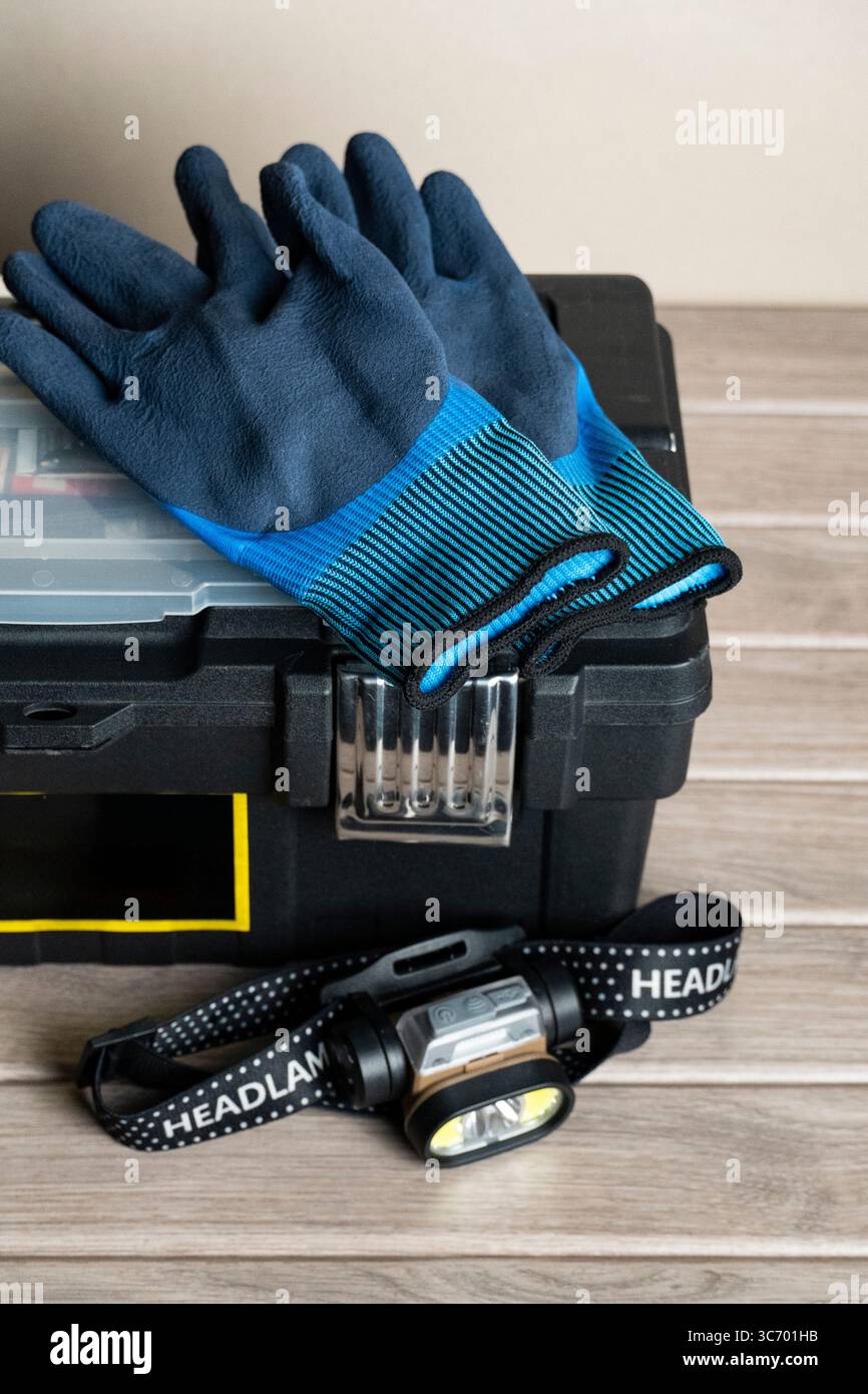 Primo piano di una cassetta degli attrezzi nera contenente guanti blu e un faro, ideale per il fai da te, la riparazione e i lavori all'aperto Foto Stock