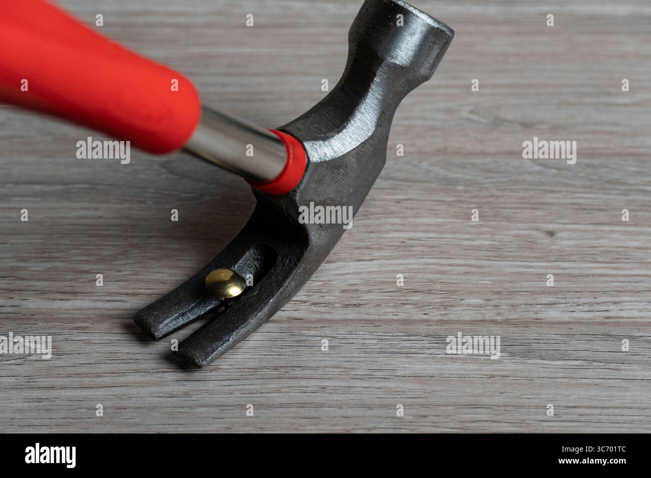 Immagine ravvicinata di un martello a baionetta con impugnatura rossa che aggancia un chiodo in ottone su una superficie in legno Foto Stock