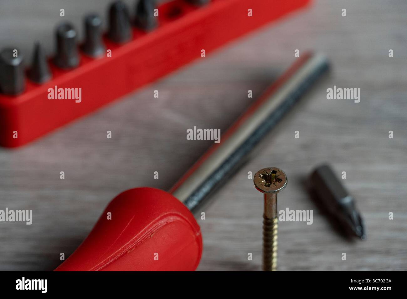 Primo piano dettagliato di un cacciavite con manico rosso, vite e punte intercambiabili su una superficie in legno. Perfetto per il fai da te, l'hardware e la grafica di riparazione Foto Stock