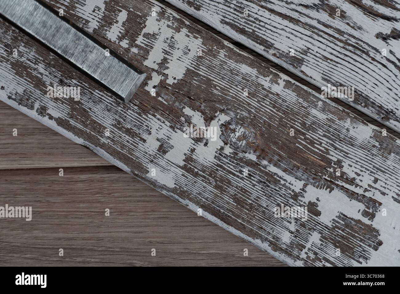 Una vista ravvicinata delle tavole di legno intemperie con vernice bianca sbucciante e scalpello metallico, che mostra fascino rustico ed estetica vintage Foto Stock