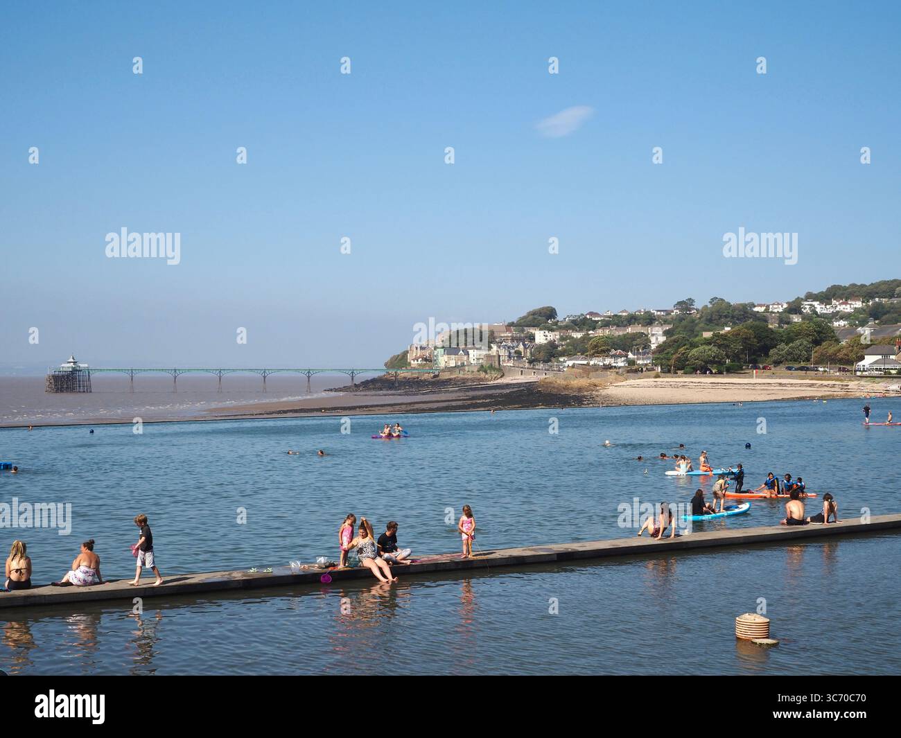 Persone che pagaiano, prendono il sole e fanno kayak al Clevedon Marine Lake, North Somerset, con Clevedon Pier sullo sfondo. Estate, sport acquatici, kayak. Foto Stock