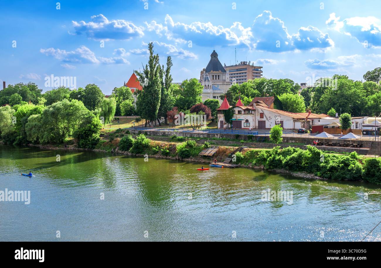 Arad, Romania - Vista panoramica del fiume Mures con architettura storica e vegetazione lussureggiante in una giornata di sole Foto Stock