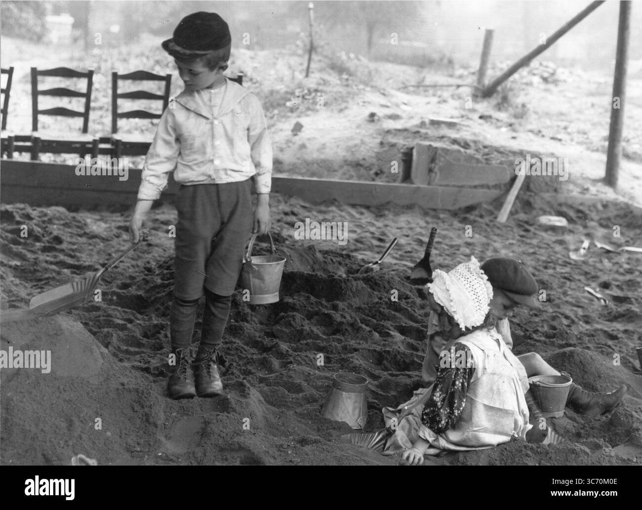 Bambini edoardiani che giocano con secchio di metallo e vadano in sabbia , scavando e facendo castelli di sabbia . 1910 Foto Stock