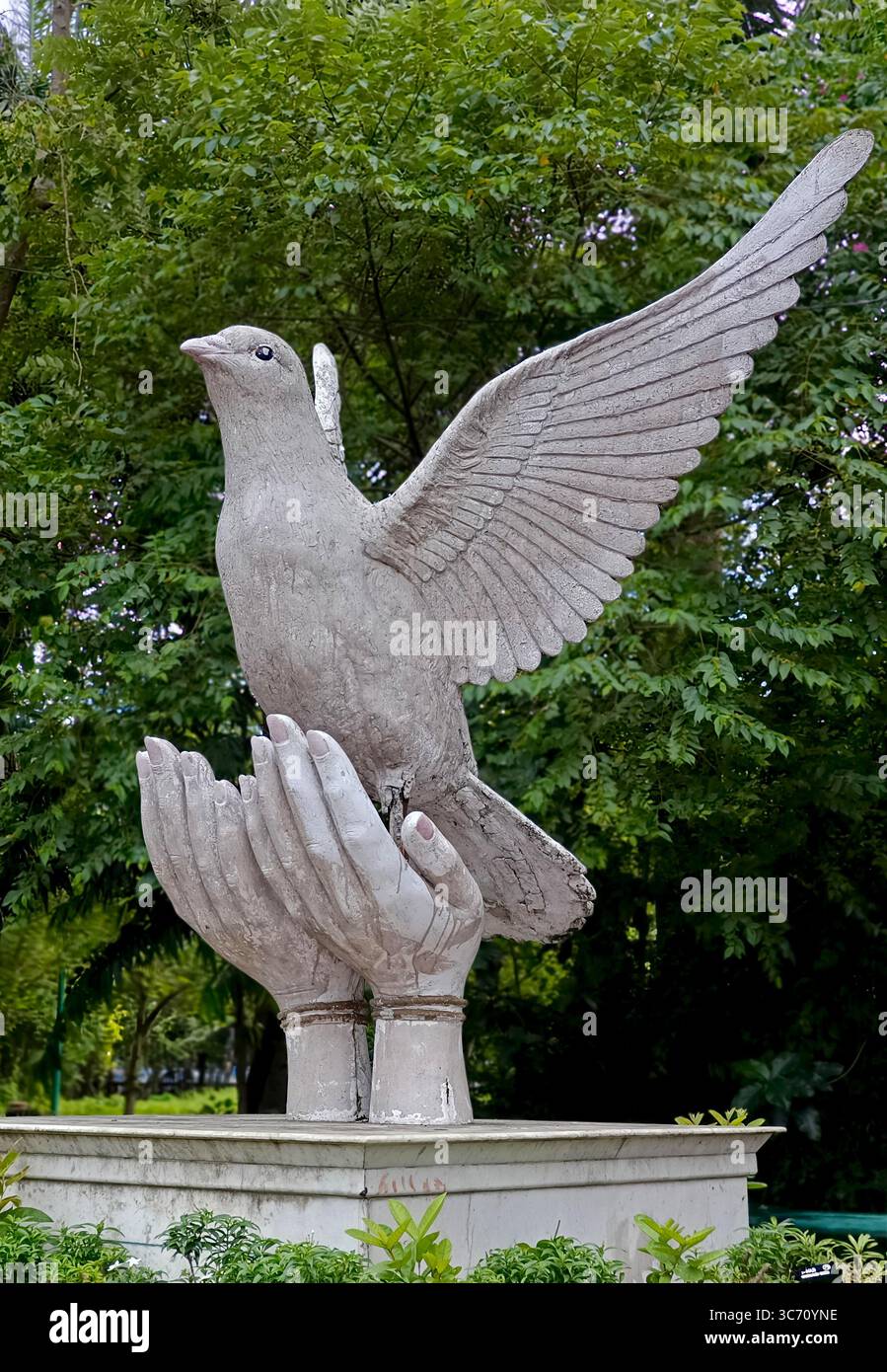Scultura di una colomba che prende il volo da un paio di mani, simboleggia la pace e la libertà, situata in un lussureggiante parco verde in India. Foto Stock