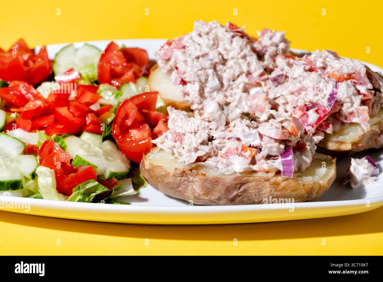 Un'insalata di tonno in scatola servita su un piatto. Il tonno viene servito su una patata al forno con un'insalata di foglie verdi fresche. Un pasto sano Foto Stock