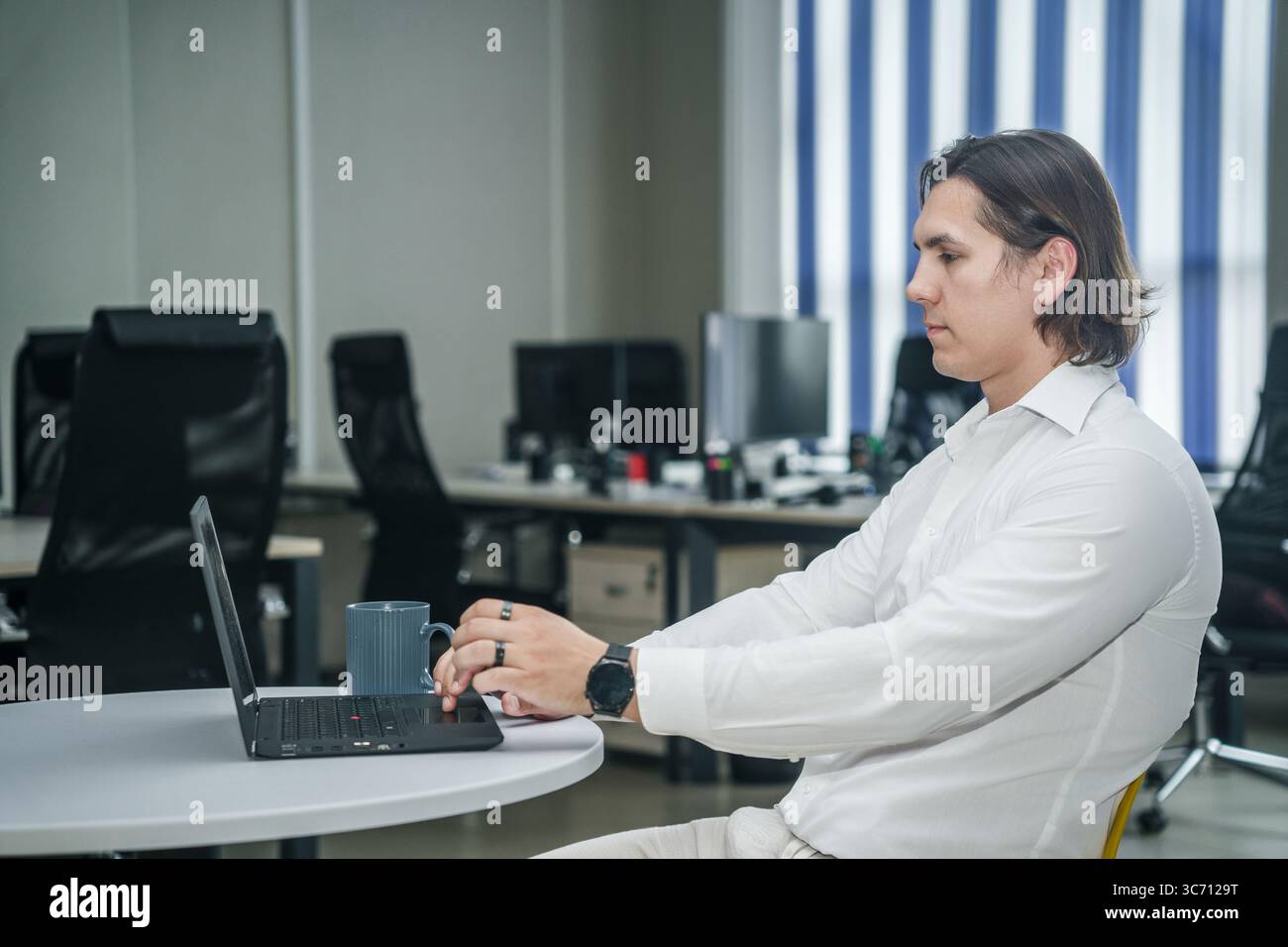 L'uomo lavora con un computer portatile con caffè in un ufficio moderno e luminoso. Foto Stock