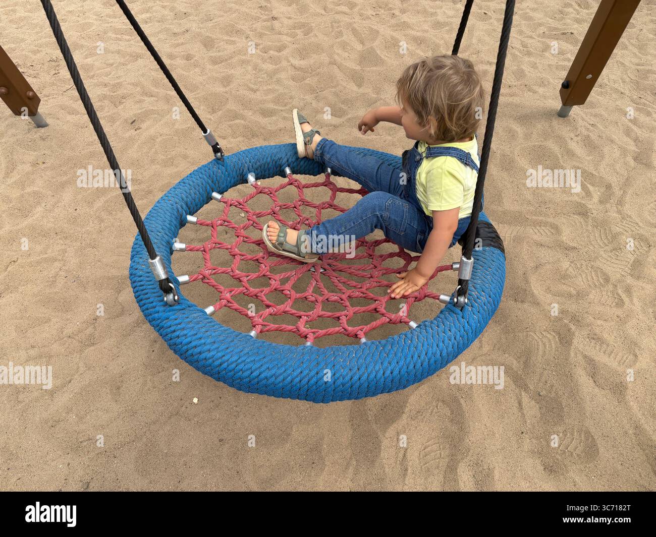 Bambino seduto su un'altalena di corda al parco giochi. Gioco all'aperto attivo, sviluppo dell'equilibrio e capacità motorie lorde nella prima infanzia. Foto Stock