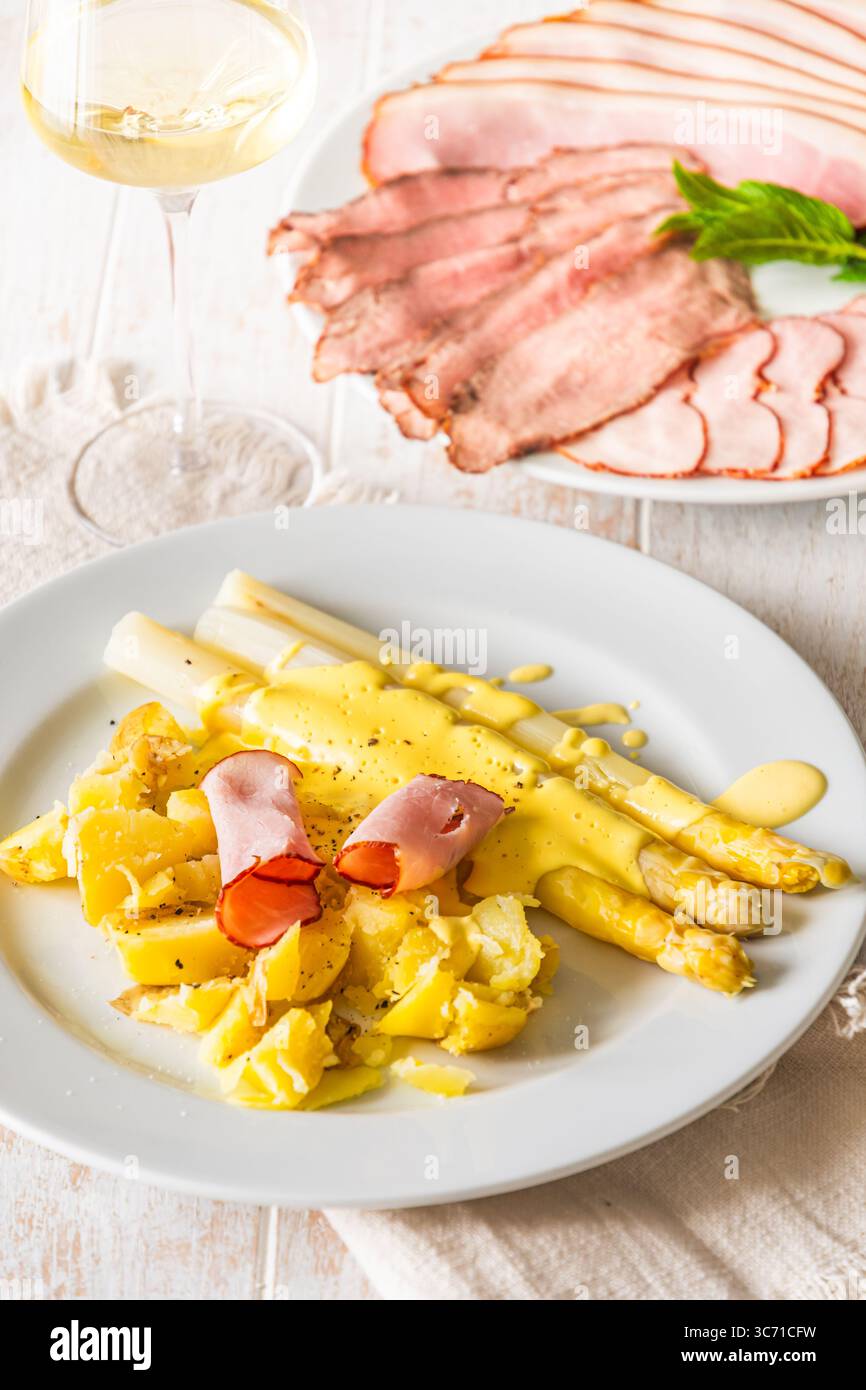 Piatto con asparagi, patate, prosciutto e salsa hollandaise su fondo di legno bianco, verticale Foto Stock