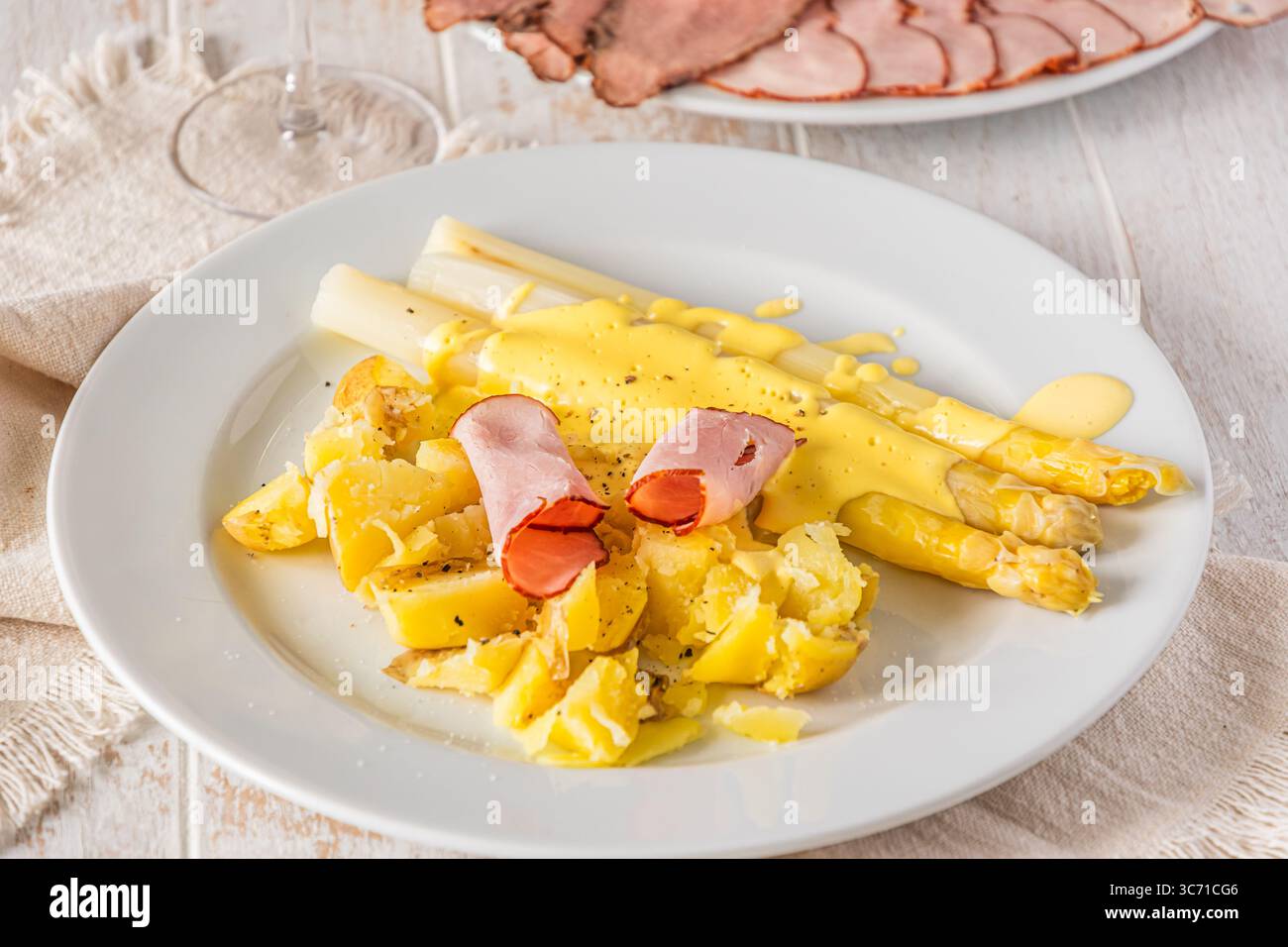 Piatto con asparagi, patate, prosciutto e salsa hollandaise su sfondo bianco di legno Foto Stock