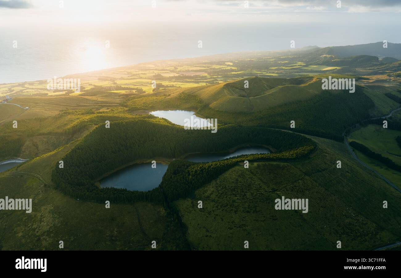 Vista aerea dei laghi gemelli annidati nel verde del cratere vulcanico, illuminati dal sole dorato contro l'orizzonte lontano, São Miguel Island, Az Foto Stock