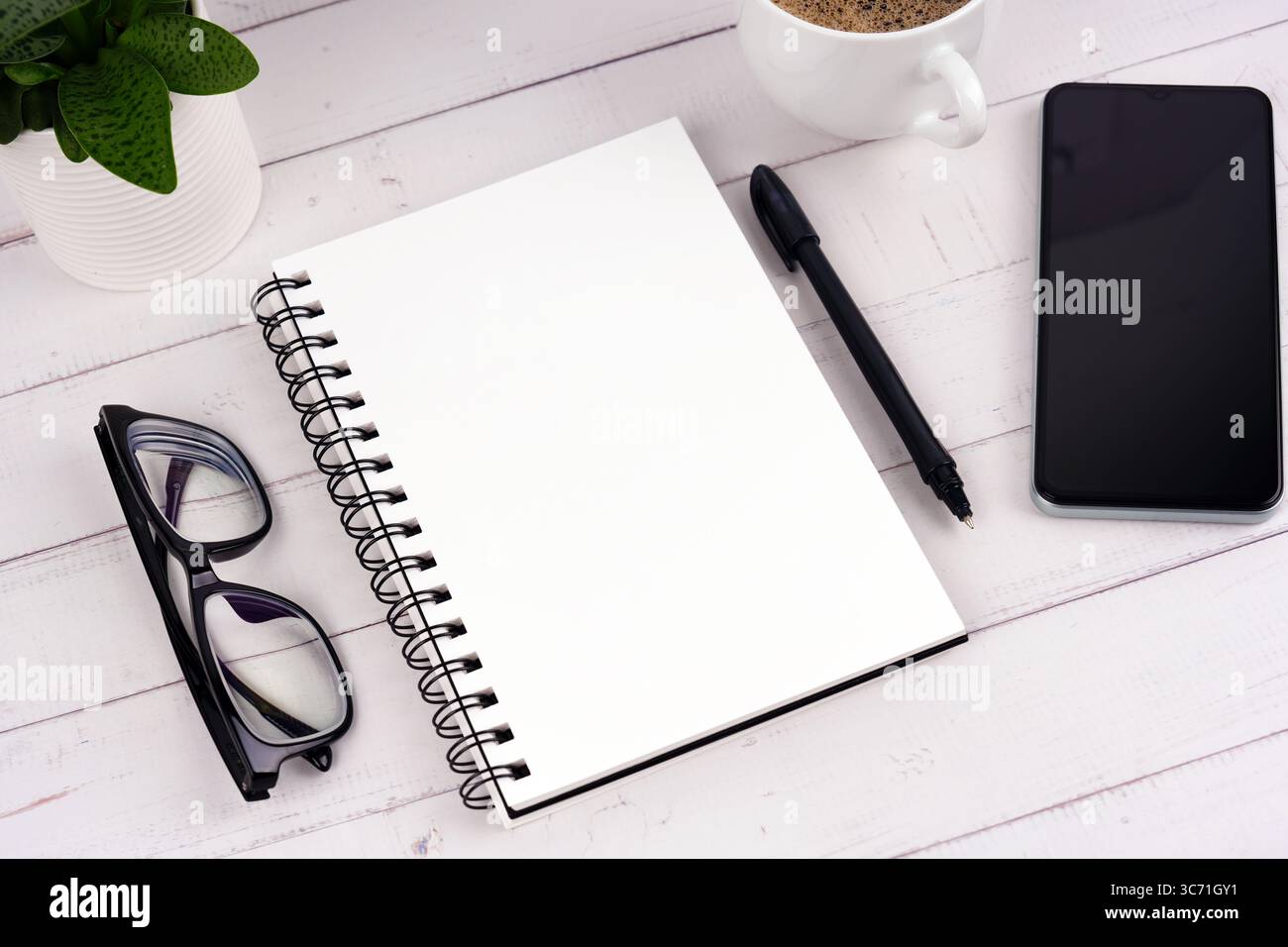 Blocco note, smartphone e occhiali vuoti su una scrivania piatta Foto Stock