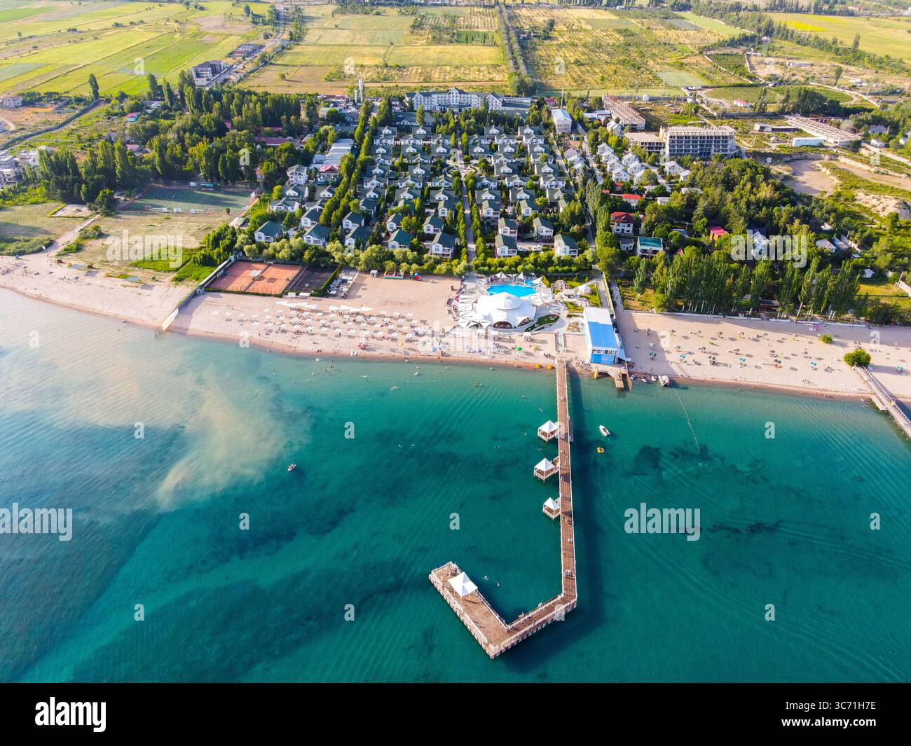 Ampia vista aerea di un resort sul lago con un lungo molo che si estende nelle acque turchesi e una grande piscina sulla spiaggia Foto Stock