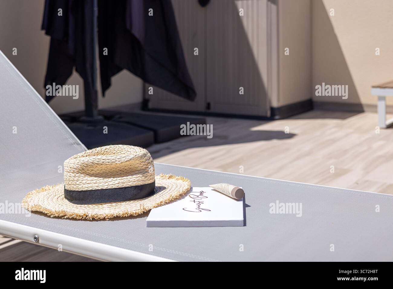 Cappello di paglia e libro posti su un lettino, evocando un'atmosfera di vacanza tranquilla. Foto Stock