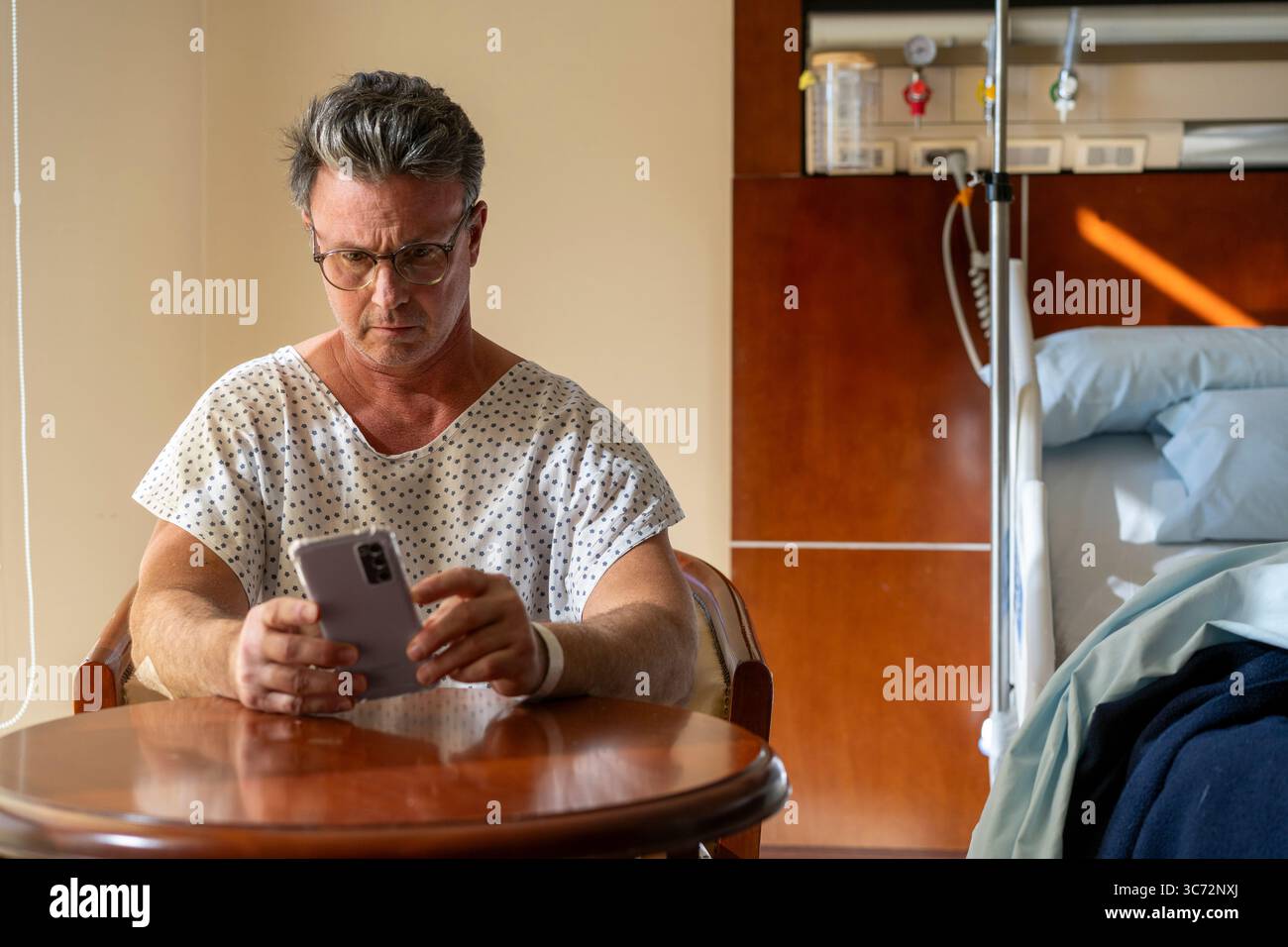 Paziente ricoverato che controlla il telefono in camera privata. Foto Stock