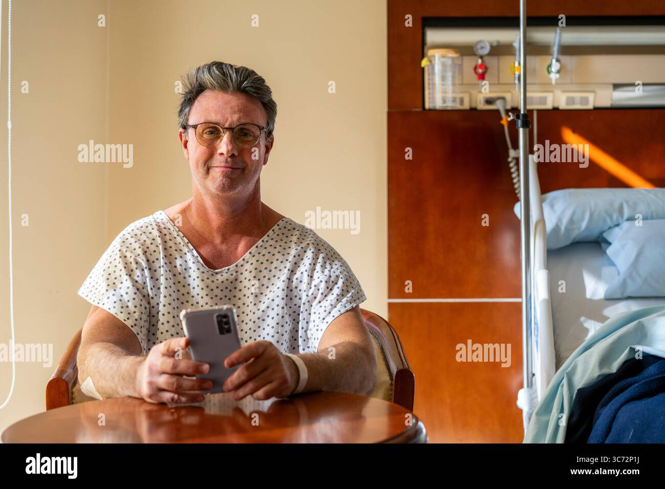 Paziente ricoverato che tiene il telefono mentre guarda la fotocamera. Foto Stock