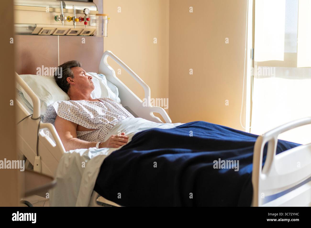 Uomo ricoverato in ospedale che si riprende e osserva attraverso la finestra. Foto Stock