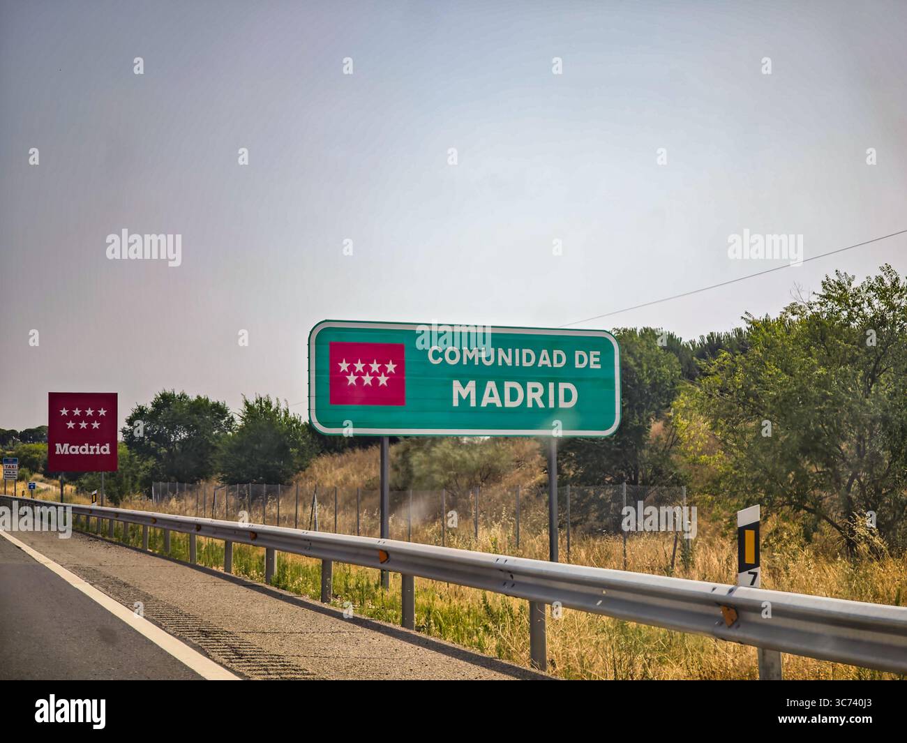 Un chiaro cartello stradale accoglie i viaggiatori al Comunidad de Madrid, circondato da vegetazione e campi in una giornata di sole. Foto Stock