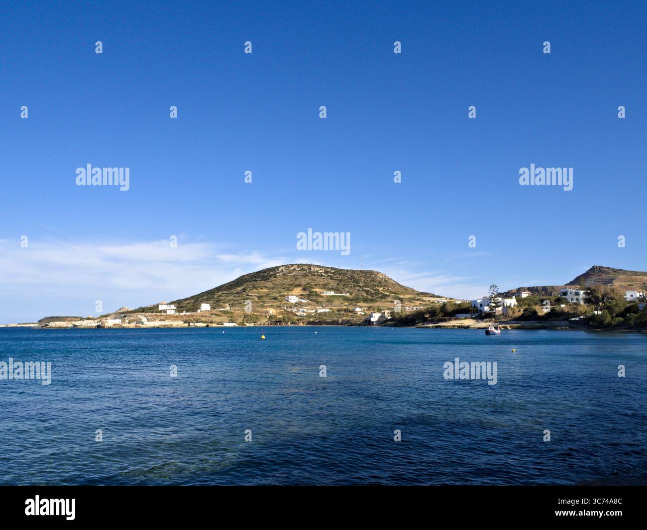 Panorama costiero vicino ad Apollonia sull'isola di Milos, in Grecia: Le case bianche in cima alla collina si affacciano sul Mar Egeo sotto un vivace cielo blu. Foto Stock