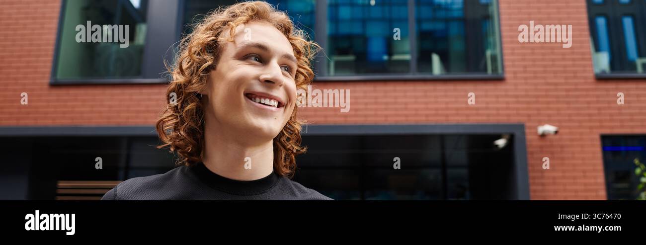 Una persona sportiva con i capelli ricci sorride mentre si trova all'esterno di edifici contemporanei in città. Foto Stock