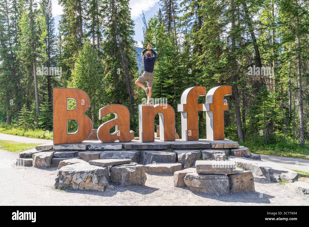La posa dell'albero di Banff Yoga è dimostrata presso l'iconico cartello Banff nel Parco Nazionale di Banff. Il parco, fondato nel 1885, è noto per il suo territorio montuoso Foto Stock
