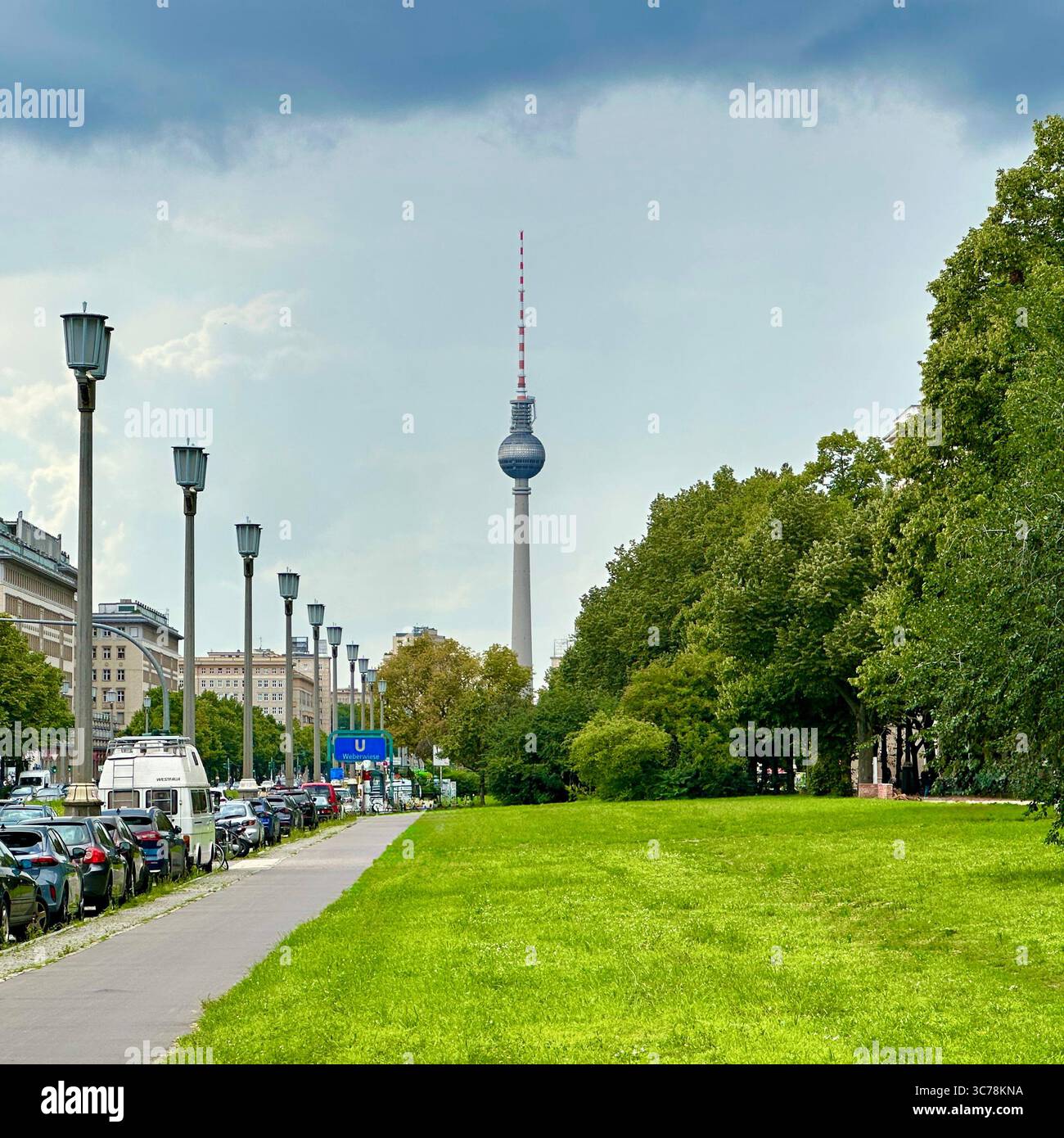 L'iconica torre della televisione di Berlino (Fernsehturm) vista dallo storico Karl-Marx-Allee. L'ampio viale è caratterizzato da un parco lussureggiante e dalla classica strada della DDR Foto Stock