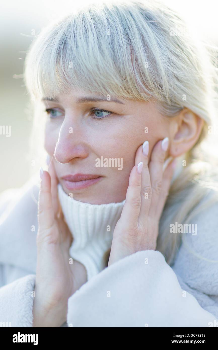 Ritratto ravvicinato di una donna matura triste con i capelli bianchi, che tiene il viso con le mani, soffre di mal di denti o depressione Foto Stock