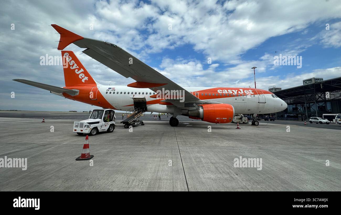 EasyJet Airbus A320 parcheggiato in grembiule all'aeroporto di Salonicco sotto cielo limpido con attività a terra estiva visibile. Foto Stock