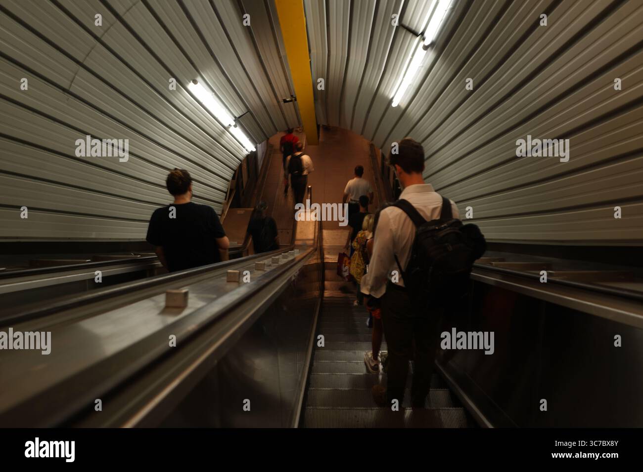 I passeggeri scendono su scale mobili in una moderna stazione della metropolitana di Roma. Il tunnel metallico a costine crea uno sfondo futuristico per il corvo in movimento Foto Stock