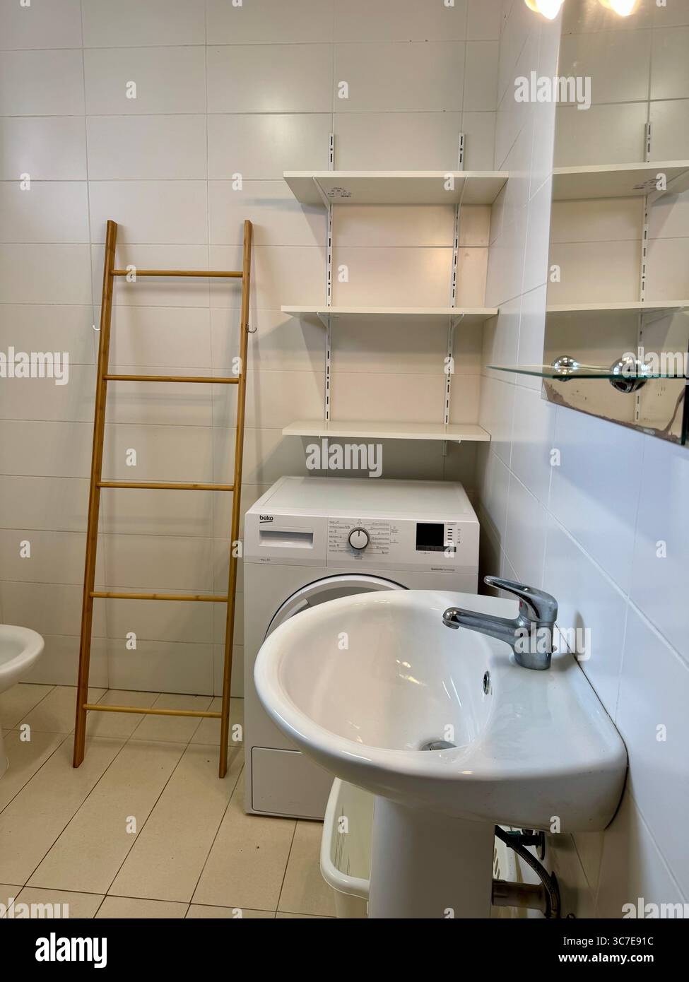 bagno moderno e pulito con piastrelle bianche, cabina doccia, wc, bidet, lavandino, e scaffali. Foto Stock