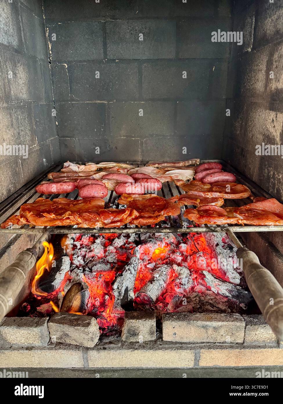 Salsicce e costolette cucinate su carboni caldi accesi su un barbecue. - Immagine stock catturata con smartphone