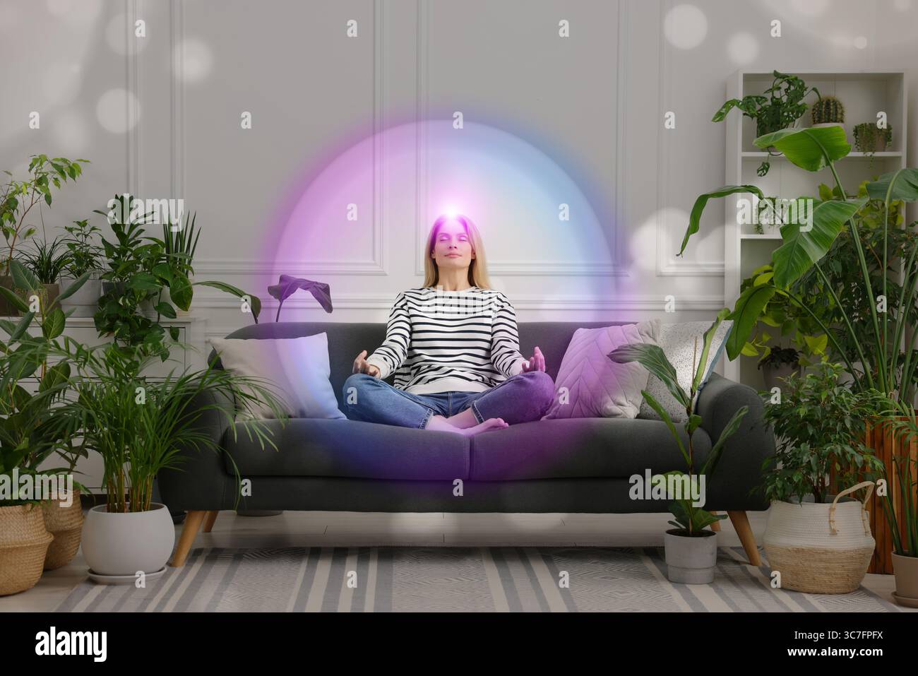 Donna che meditava in posa Lotus a casa. Una bolla luminosa intorno a lei che rappresenta l'aura Foto Stock