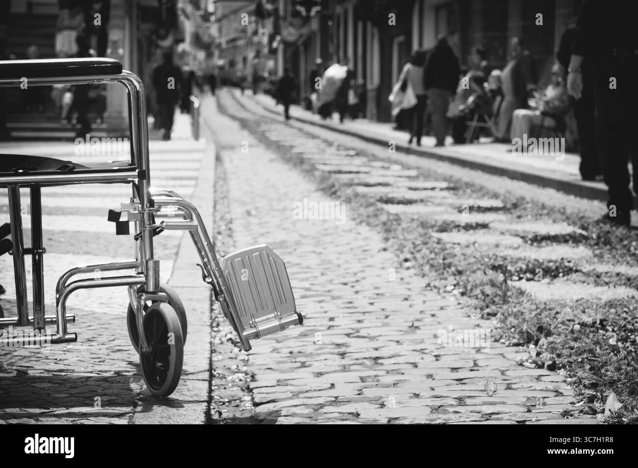 Immagine concettuale in bianco e nero di una sedia a rotelle vuota lungo il percorso della processione dell'Ecce Homo a Ponta Delgada, Azzorre, che simboleggia la guarigione del thro Foto Stock