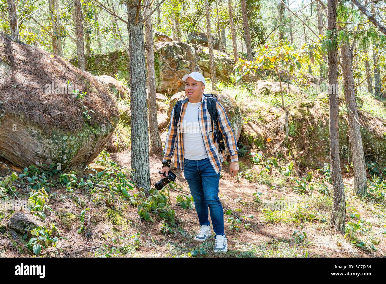 Il fotografo maschile latinoamericano si trova nella foresta, osservando attentamente il paesaggio alla ricerca della prossima foto. Un momento tranquillo e premuroso ideale Foto Stock