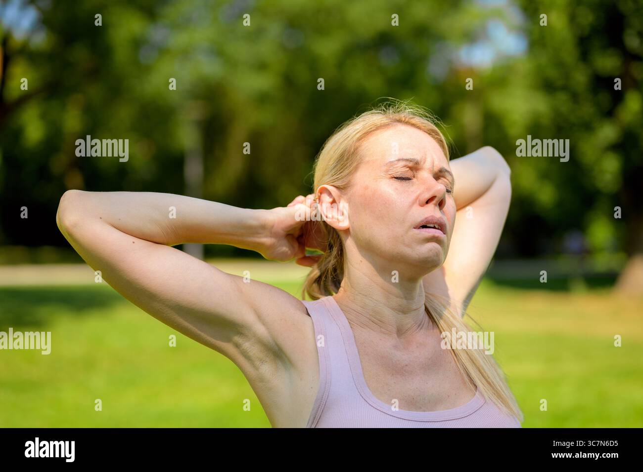 Primo piano di una donna bionda in una canotta rosa in un parco illuminato dal sole. Foto Stock Primo piano di una donna bionda in una canotta rosa in un parco illuminato dal sole. Foto Stock