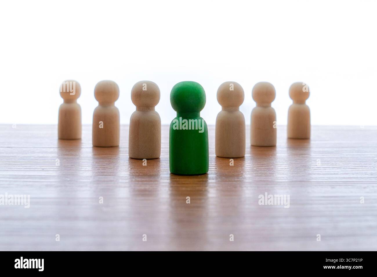 Una bambole di legno si staglia su una superficie di legno con una bambola verde al centro. Leadership, diversità, individualità. Foto Stock