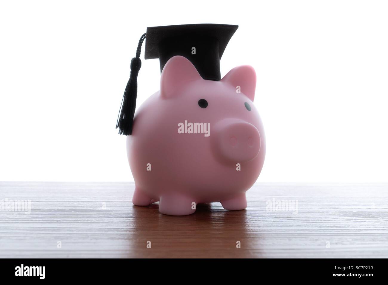Un salvadanaio che indossa un berretto nero graduato con una nappina. Investimenti finanziari nell'istruzione, risparmio per la scuola, prestiti per gli studenti. Foto Stock
