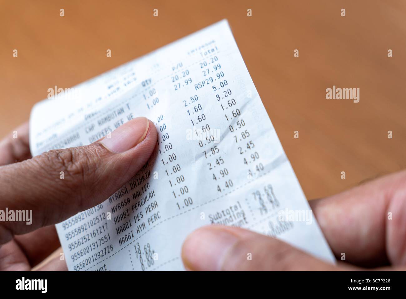 Le mani di una persona stanno reggendo ed esaminando una lunga ricevuta stampata della spesa. Shopping, spese, concetto di budget. Foto Stock