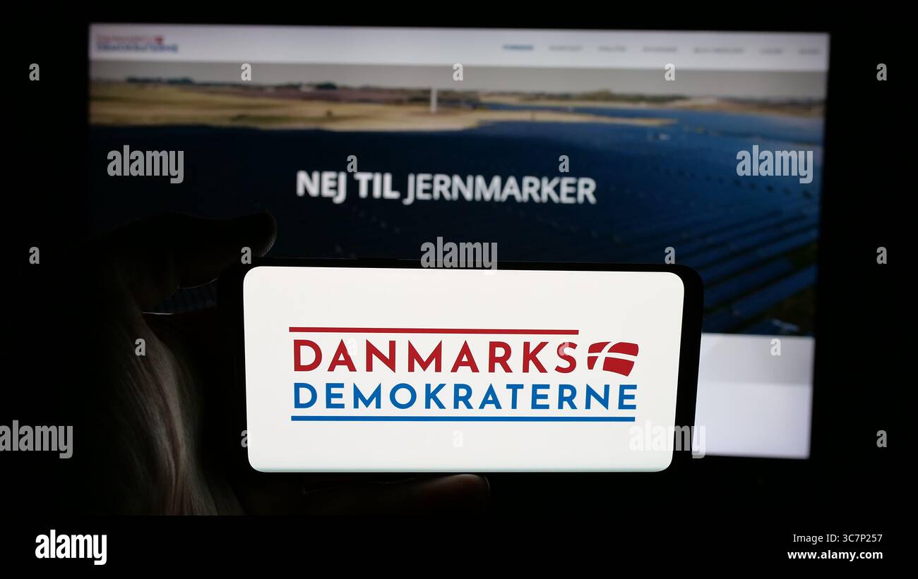 Stoccarda, Germania - 07-11-2025: Persona che tiene il cellulare con il logo del partito politico danese Danmarksdemokraterne sullo schermo di fronte alla pagina web. Foto Stock