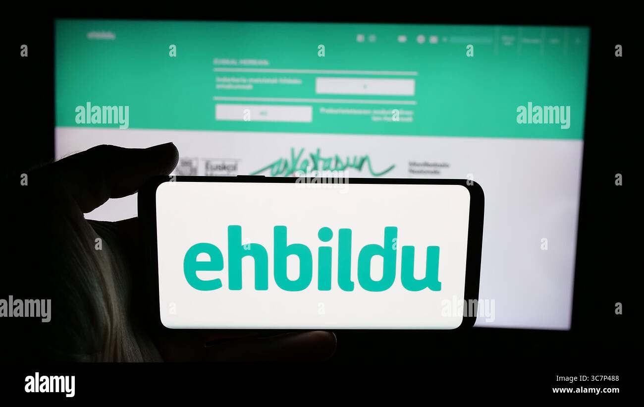 Stoccarda, Germania - 07-18-2025: Persona che tiene il cellulare con il logo della festa spagnola Euskal Herria Bildu (EHBildu) sullo schermo davanti alla pagina web. Foto Stock