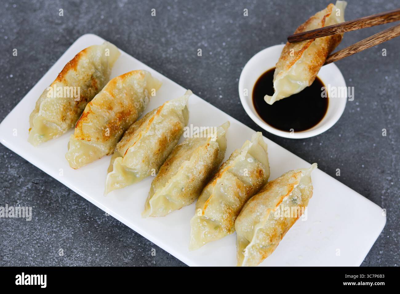 Un paio di bacchette che immergono gnocchi Mandu o coreani in una piccola ciotola di salsa di soia scura. Foto Stock