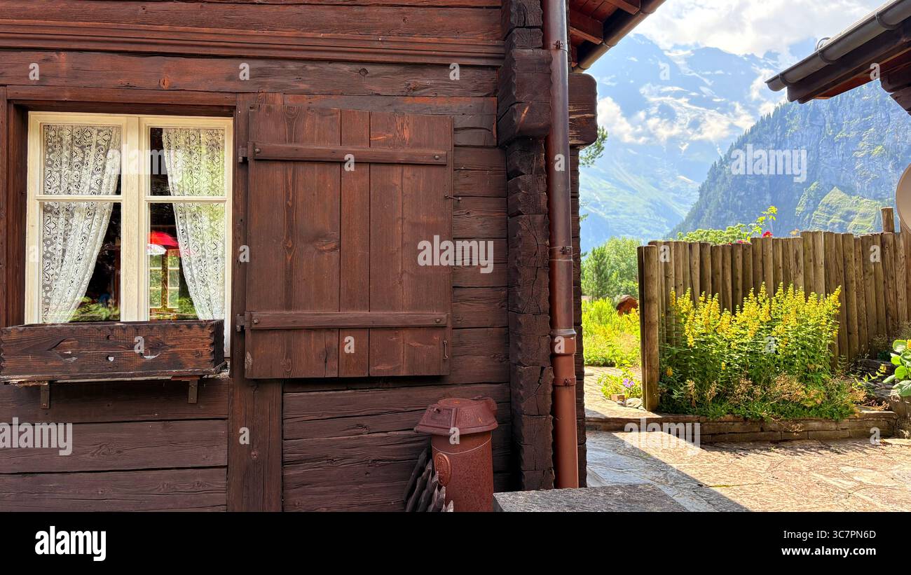 Finestra di chalet rustico in legno con tende in pizzo, paesaggio montano e giardino nelle Alpi svizzere, atmosfera estiva. Foto Stock