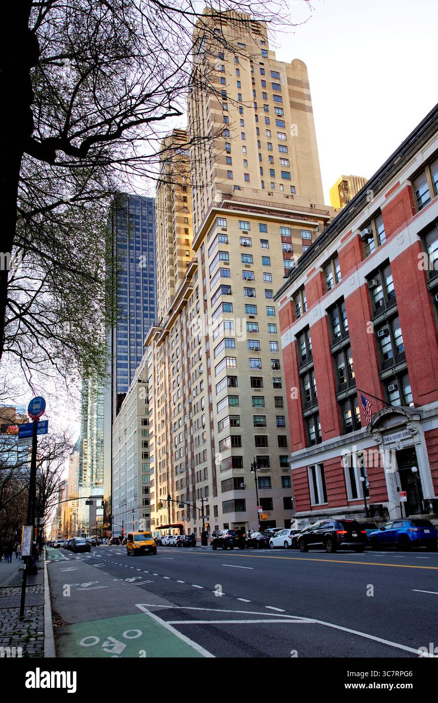 Strada alberata di Manhattan con una pista ciclabile fiancheggiata da grattacieli storici e torri moderne sotto un cielo invernale blu cristallino a Midtown, alla luce del sole. Foto Stock