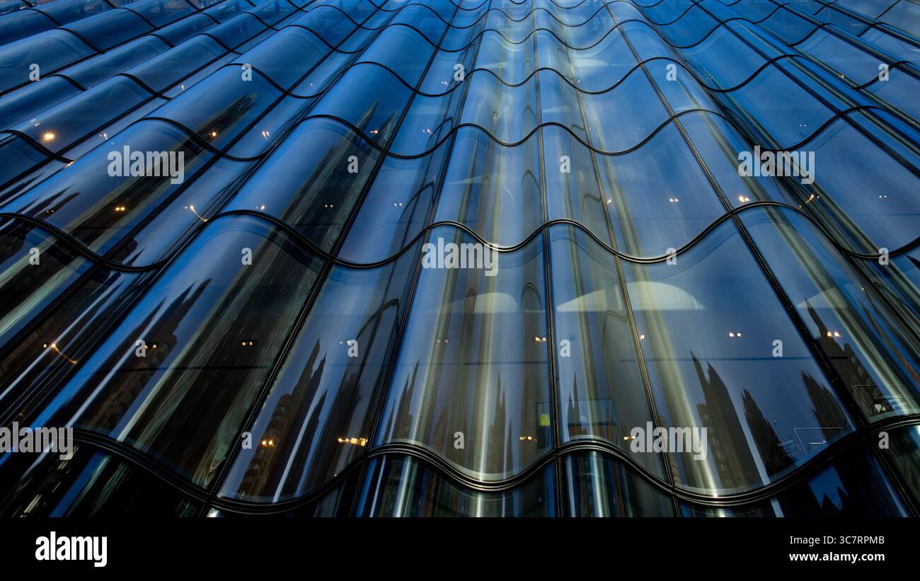 Ammira una cortina di vetro ondulata su un grattacielo di Manhattan che si estende verso il cielo, con i suoi pannelli rifrangenti che scintillano nella vita cittadina. Foto Stock
