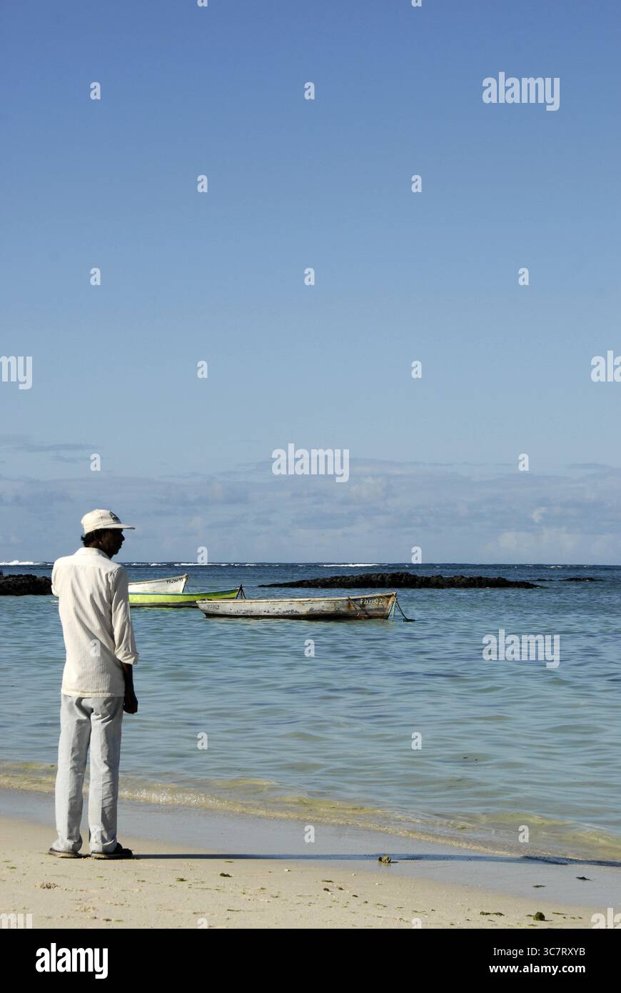 Un uomo anziano osserva le barche ormeggiate vicino alla riva a Mauritius, marzo 2017. Una tranquilla scena costiera. Foto Stock