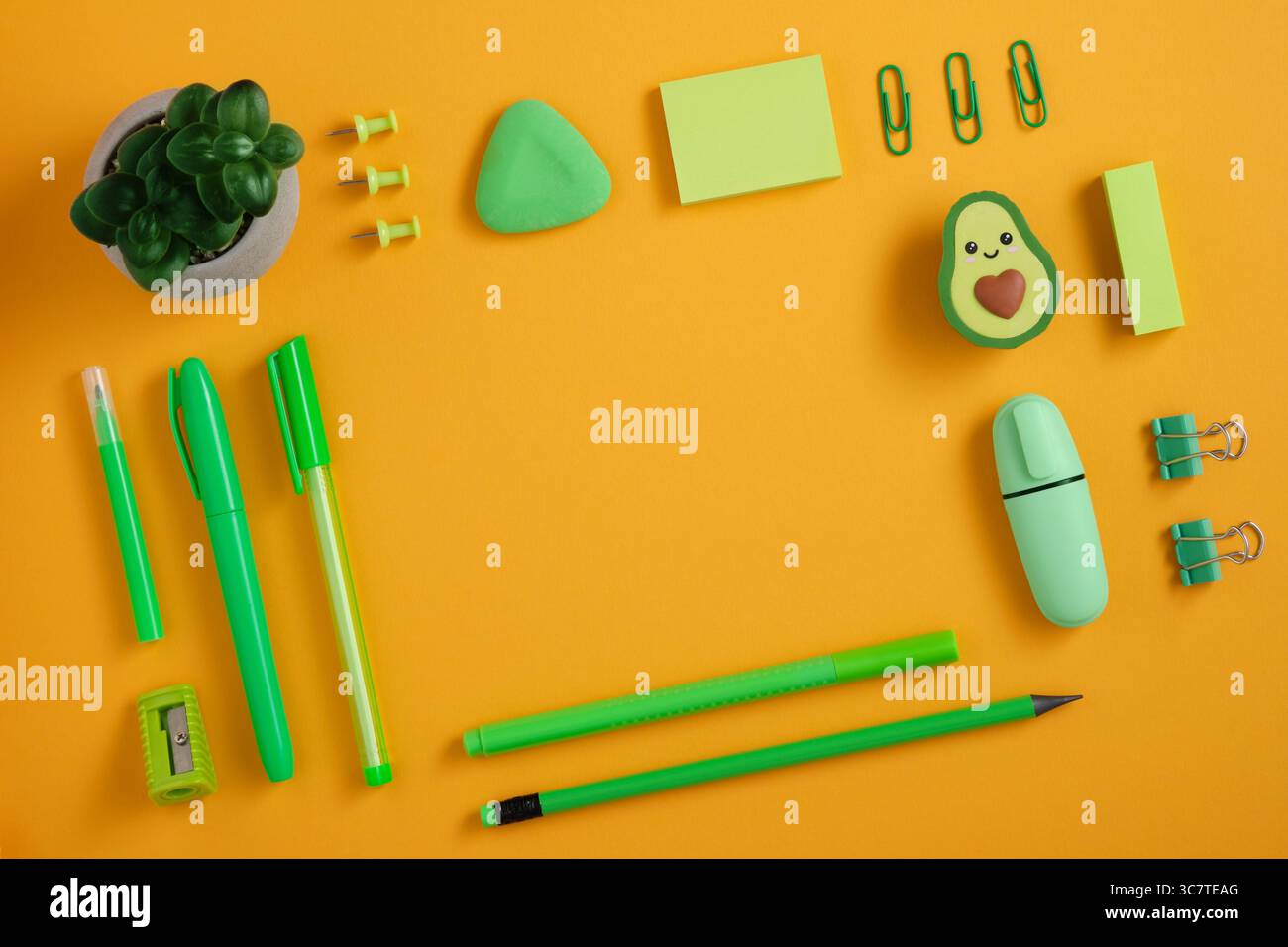 Cornice di penna verde, matita e pennarello su sfondo giallo. Gomma a forma di avocado. In piano. Foto Stock