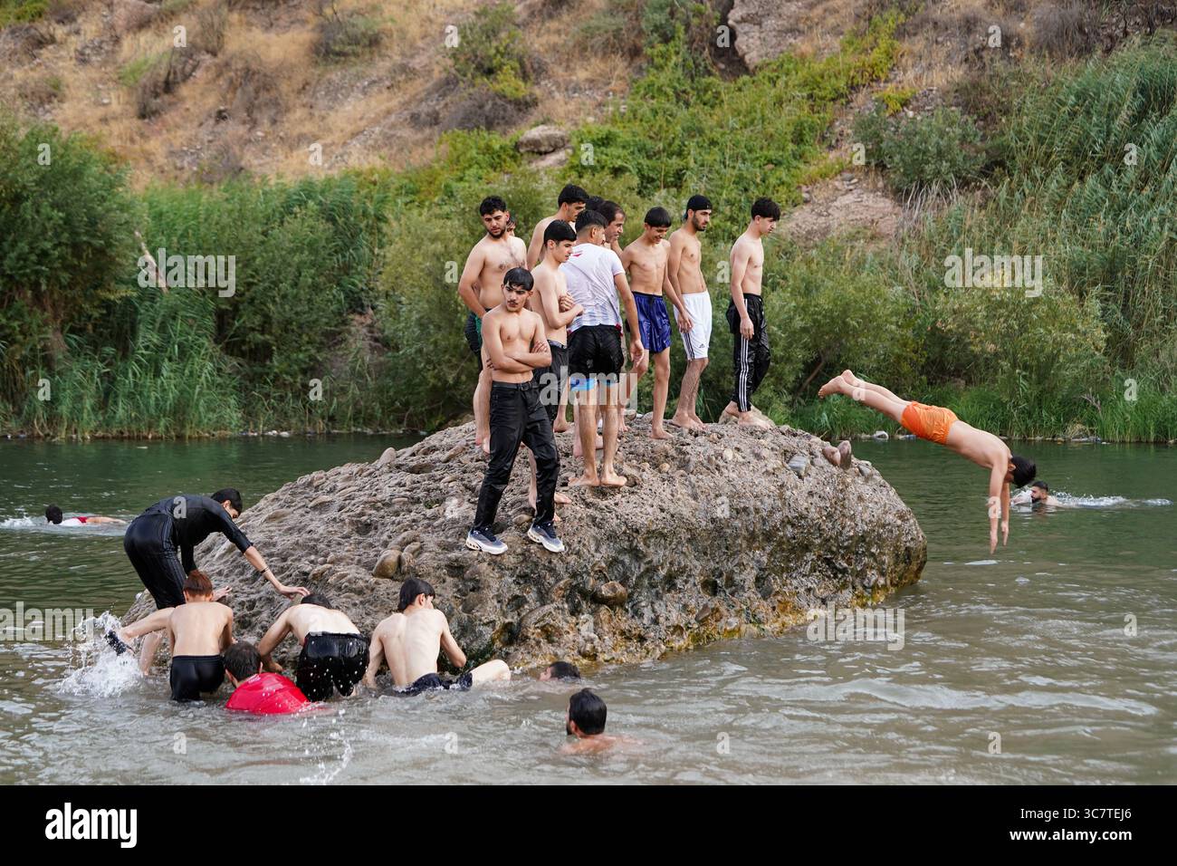 Zakho, Iraq. 1 agosto 2025. Giovani uomini si alzano su una roccia nel fiume Khabur prima di saltare in acqua nella regione del Kurdistan. Un'ondata di calore si sta diffondendo nella maggior parte delle città con temperature che raggiungono circa 50 gradi Celsius. (Foto di Ismael Adnan/SOPA Images/Sipa USA) credito: SIPA USA/Alamy Live News Foto Stock