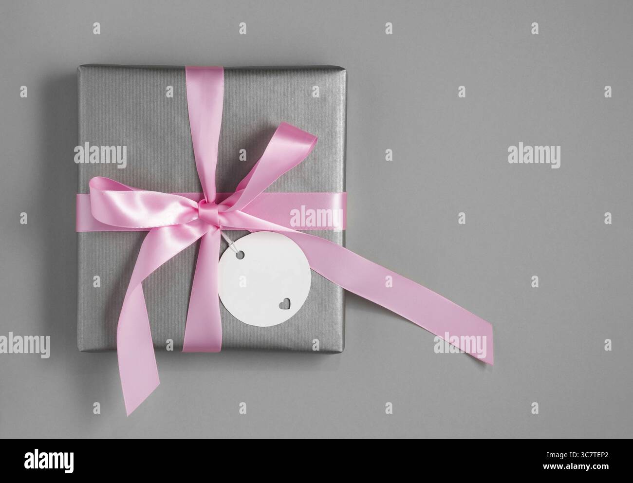 Confezione regalo argento con nastro rosa e targhetta regalo bianca su sfondo grigio. Spazio per il testo. Foto Stock