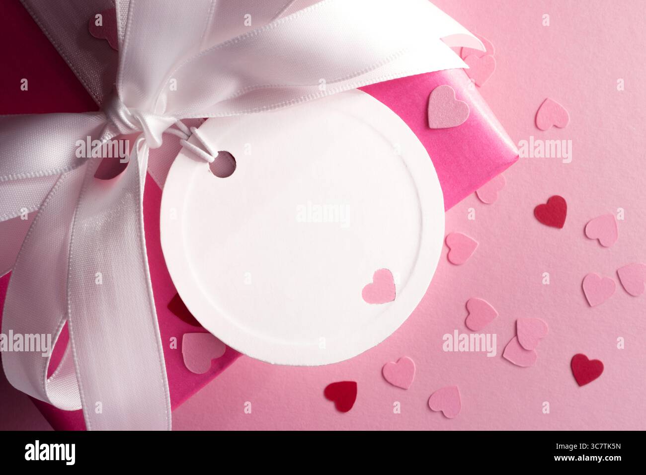 Etichetta regalo rotonda vuota con cuore su confezione regalo rosa con fiocco bianco. Spazio per il testo. Foto Stock